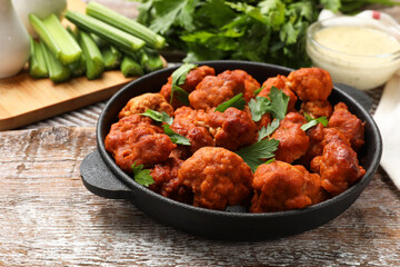 Baked cauliflower buffalo wings with parsley in baking dish on wooden table, closeup