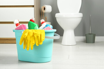 Bucket with different toilet cleaners, rag, sponge and gloves on floor in bathroom