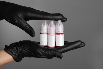 Professional cosmetologist holding bottles of pigments for permanent makeup on grey background,...