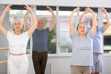 Diligent old woman doing choreography together with other elderly participants of ballet classes