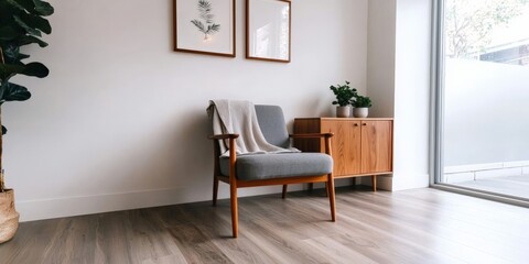 A minimalist living space featuring a sleek wooden cabinet, a gray armchair with a throw blanket, and simple decor elements like indoor plants and framed artwork, bathed in natural light