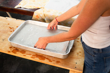 Unrecognizable woman showing the process of making handmade recycled paper putting paper pulp in frame mold. Reusable and renewable material concept.