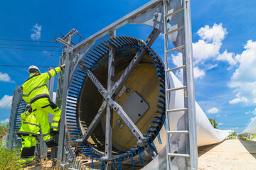 Two engineers in safety gear inspecting a wind turbine blade section on a construction site. They examine the metal framework with precision. Renewable energy project under a clear blue sky.