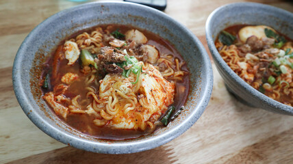 Mie Kuah or Instant noodle soup topped with pokcoy, eggs, meatballs, chopped green onions and chili pieces. served on blue bowl isolated on wooden table