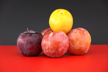 Colorful plums displayed on a bold red surface against a dark background