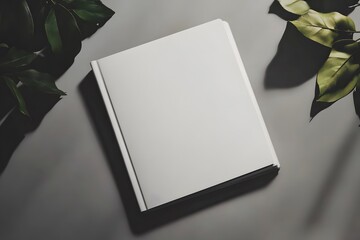 A blank, open book rests on a surface surrounded by green leaves, offering a serene and minimalist aesthetic ideal for creativity and inspiration.