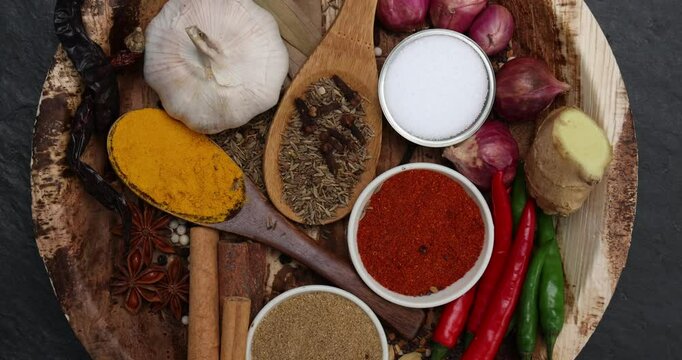 Asian favour spice green red dry chilli powder onion garlic ginger cinnamon cardamon turmeric fennel seeds bay leaf clove star anise wooden spoon blows on palm leaf plate over black slate background