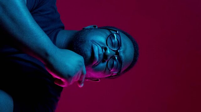 Vertical video. Question puzzled. Choice decision. Uncertain doubtful man with pensive facial expression pointing finger in neon light isolated on burgundy background copy space.