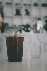 Ice Americano coffee in plastic coffee cup on white table served with cool water.