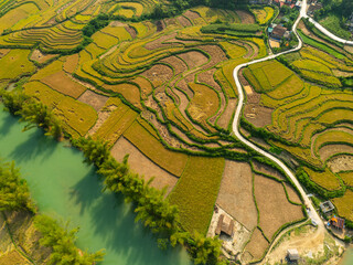 A stunning aerial view of a small rural village nestled on the banks of a winding river, surrounded by lush rice fields and natural waterfalls in a verdant landscape.
