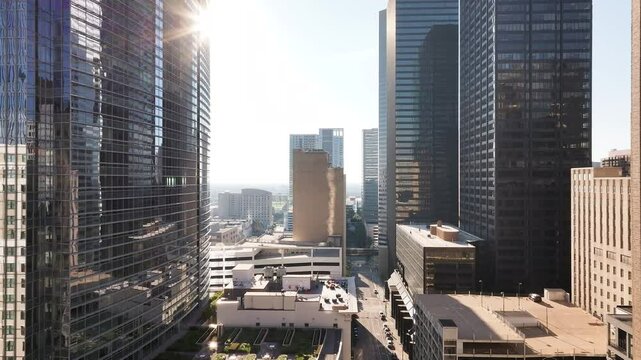Drone view flying through misc tall buildings in downtown Houston, Texas with a sun reveal and smoke coming up from a building.