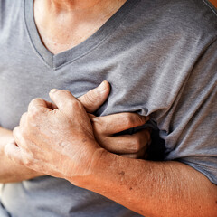 Fototapeta premium elderly person in gray shirt clutches their chest, possibly indicating discomfort or pain. image conveys sense of urgency and concern