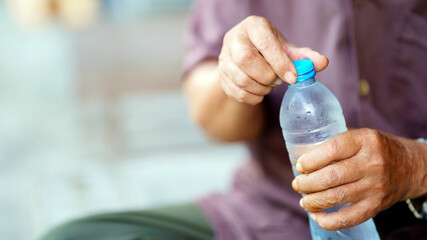 person opening cold water bottle, focusing on hands and bottle, outdoors. image captures moment of refreshment and hydration