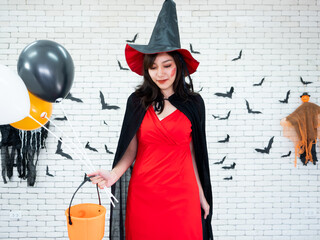 Asian cheerful woman dressed as a witch, holding orange, black and white balloons with a pumpkin...