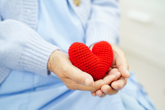 Asian elder senior woman patient holding red heart in hospital.