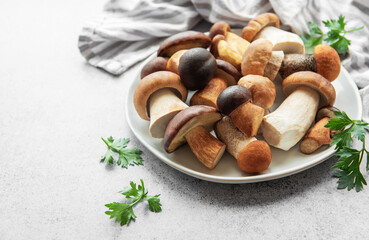 Freshly gathered assorted mushrooms on a plate with herbs set on a gray countertop for culinary preparation