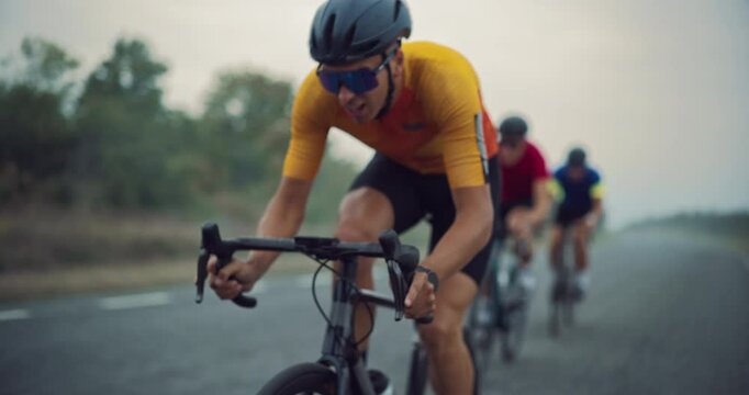 Close Up of an Exhausted Determined Professional Cyclist Riding in Front of the Pack, Battling for the Win in the Race. Competitors Drafting Behind, Ready to Overtake on an Open Misty Road