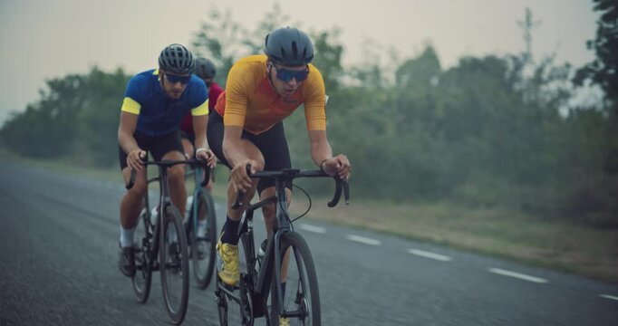 Cyclist Team of Three Men Rides Along the Open Road, Cloudy Sky Above Matching the Serious Mood of Their High-Intensity Practice. Riders Work in Tandem, Switching Leaders to Preserve Momentum
