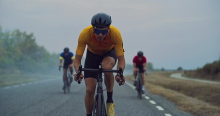 Male Cyclist Sets the Pace, Riding Strongly in Front While Two Teammates Follow Behind Side by Side. Athletes Ride Together, Their Focus Intense as They Tackle the Misty Road Ahead