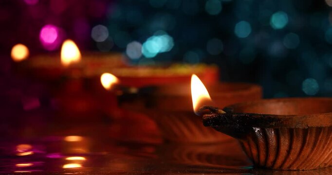 Lit traditional clay oil lamps are lined up with light reflections on a background of pink and blue bokeh effects.