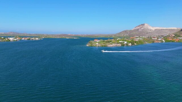 Aerial view of single speed boat racing across a coastal bay with turquoise waters and scenic hills in the background