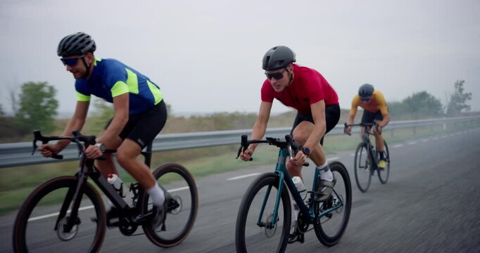 With Determined Expression Athlete Overtakes the Leader of the Pack During a Bicycle Race. Three Cyclists Ride Along the Road, Bikes Cutting Through the Wind on a Cloudy Moody Afternoon