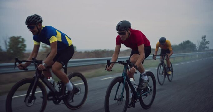 Cyclist Team of Three Men Rides Along the Open Road, Cloudy Sky Above Matching the Serious Mood of Their High-Intensity Practice. Riders Work in Tandem, Switching Leaders to Preserve Energy