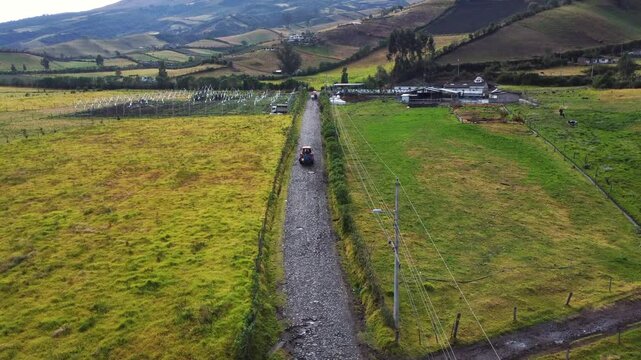 Aerial view of a tranquil countryside road surrounded by green fields and rolling hills in romerillo sector, Machachi parish, Mejia canton, Pichincha, Ecuador with Rumi&ntilde;ahui volcano in the background