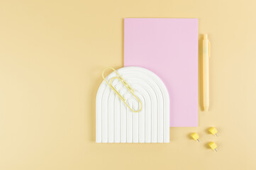 Top view of pink notebook, yellow pen, paperclip, pins, white arch tray on yellow background. School, office wallpaper. Flat lay, copy space.