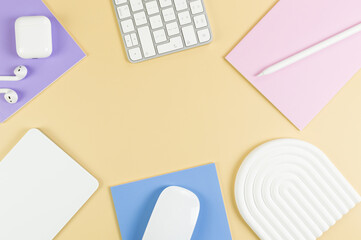 Top view of white keyboard, mouse, touchpad, earphones case, pen on yellow background. Purple, pink and blue notebooks, modern office, school. White arch tray, flat lay, copy space.