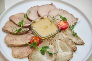 A plate of meat with a glass of sauce and a spoon. The meat is sliced and arranged in a circle