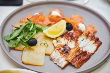A plate of food with a variety of fish and vegetables. The plate is white and the food is arranged in a visually appealing manner
