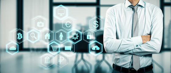 Close up of businessman with folded arms and digital business interface hologram on blurry office interior background. Technology and information concept.