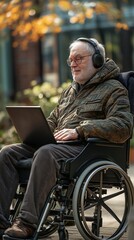 Elderly disabled man using a wheelchair, laptop, and headphones.