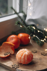 Christmas composition with tangerines and fir branches. Mandrinas lie on a wooden board, next to wooden snowflakes, fir branches and Christmas lights.