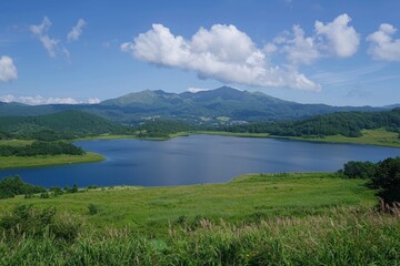 Serene lake surrounded by lush green hills and majestic mountains under a bright blue sky