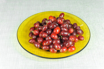 A pile of dogwood berries in a clear glass brown plate on a light surface