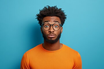 Obraz premium Man with a beard and glasses is wearing an orange shirt and looking at the camera. Concept of surprise or shock, as the man's facial expression suggests that he is taken aback by something