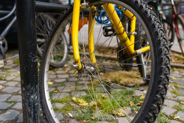 A bright yellow bike leans on a pole on an autumn cobblestone street