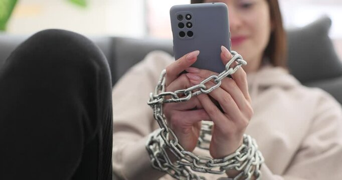 Woman with chain chained to smartphone while sitting on sofa