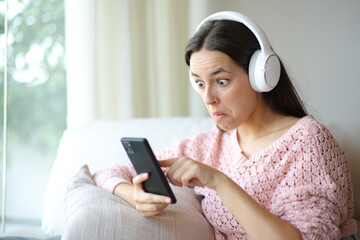 Perplexed woman listening audio with phone and headphone