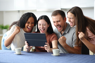Excited interracial roommates celebrating checking tablet