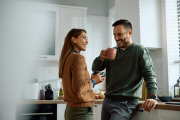 Happy couple drinking coffee while talking in kitchen.