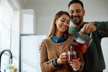 Happy man pouring cup of tea to his wife in kitchen.