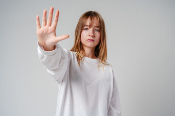 Young woman with long hair holding up her hand against a plain background