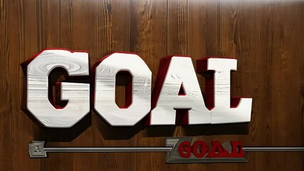 Word GOAL in varsity style, written in white with a red outline, displayed on a wooden homogeneous background resembling a locker room wall, representing motivation and the pursuit of athletic achieve