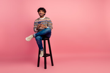 Full body photo of nice young man sit stool hold phone isolated on pink color background