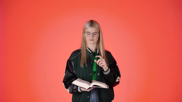 Pretty Blonde Student Making Keep Quiet Silence Gesture While Reading a Book, Studio Shot With Red Background
