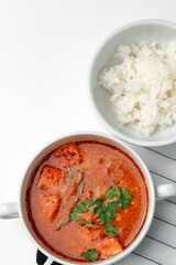Bowl of curry with pieces of meat and a side of steamed rice arranged neatly for a meal