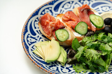 Colorful plate of smoked salmon sandwiches with cucumbers, greens, and olives on a decorative blue platter